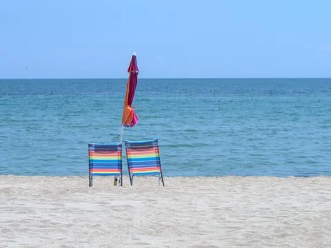 Two empty beach chairs and a closed umbrella stand on a sandy beach by the sea Stock Photos