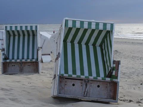 Two empty beach chairs with green and white stripe pattern standing on a sandy Stock Photos