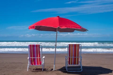 Two empty beach chairs with an umbrella on the seashore at the beach. Stock Photos