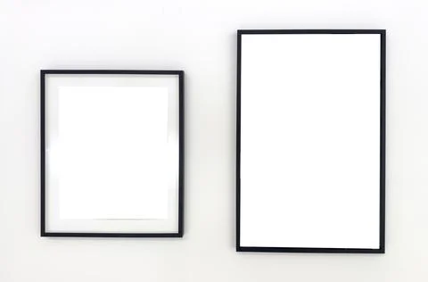 Two empty black photo frames of different sizes hanging on a white wall. Mi.. Stock Photos