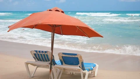 Two empty blue sun loungers under the red beach umbrella on the sand near the Stock Footage 272509148