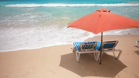 Two empty blue sun loungers under the red parasol on the sandy beach near the Video stock 272782926
