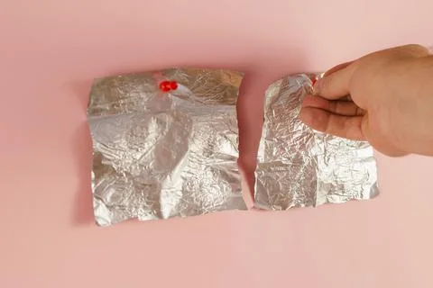 Two Empty candy wrappers pinned to a pink background. A man's hand pierces th Stock Photos