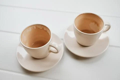 Two empty ceramic coffee cups on saucers standing on a white table after drin Stock Photos