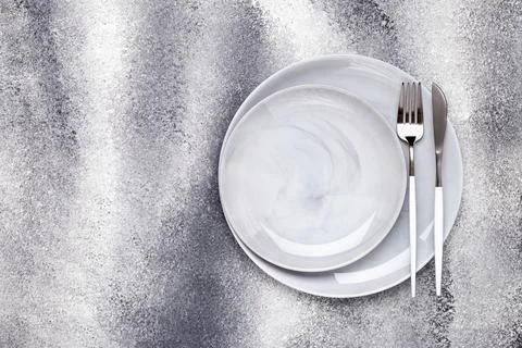 Two empty ceramics plates and unused knife with fork, crockery on a gray grun Stock Photos