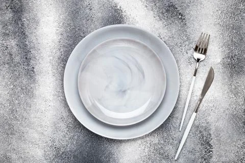 Two empty ceramics plates and clean knife with fork, crockery on a gray grung Stock Photos