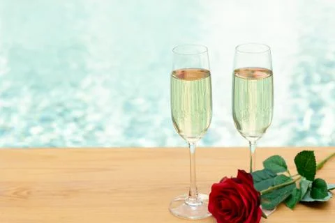 Two empty champagne glasses with rose flower next swimming pool. Stock Photos