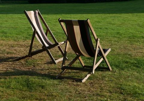 Two empty deckchairs on grass in evening sunshine with shadows Stock Photos
