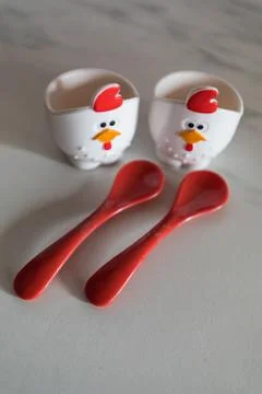 Two empty eggcups looking like a chicken with red spoons in foreground Stock Photos
