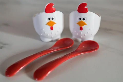 Two empty eggcups looking like a chicken with red spoons in foreground Stock Photos