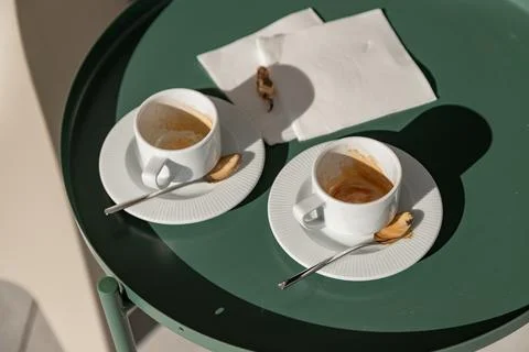 Two empty espresso cups with spoons rest on an outdoor table in warm sunlight Stock Photos