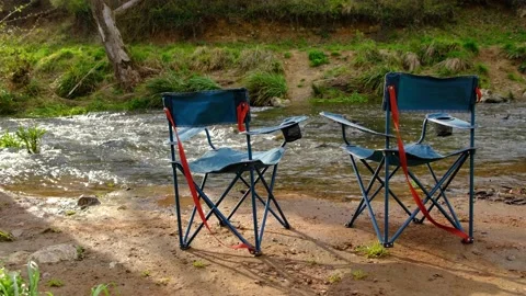 Two empty folding camping chairs near a river on a camping day. Video stock 237941030