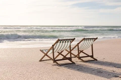 Two empty folding wooden chairs on shore at beach in front of waves splashing in Stock Photos
