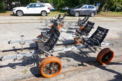 Two empty four seater rail bikes with orange wheels on a gravel parking lot Stock Photos