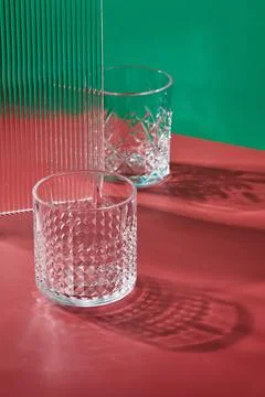 Two empty glass glasses on colored backgrounds with shadows from sunlight Stock Photos