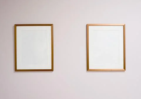 Two empty golden picture frames hanging on a blank wall, presenting a simpl.. Stock Photos