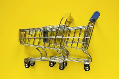 Two empty mini supermarket trolleys on a yellow background. Shopping concept. Stock Photos