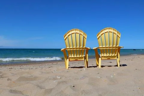 Two empty plastic yellow deck chairs facing the water on a bright sunny day Stock Photos