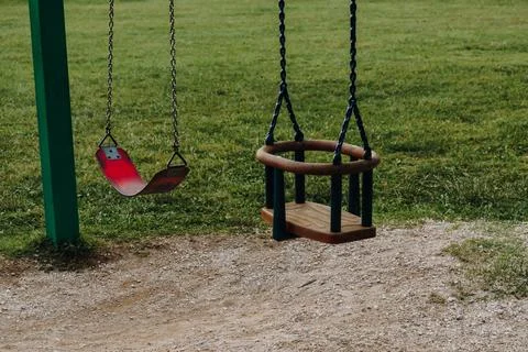 Two empty playground swings hang quietly above a grassy play area. The simp.. Stock Photos