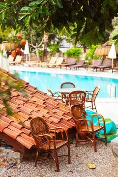 Two empty rotary stools under a tree near the pool and a tiled roof Stock Photos