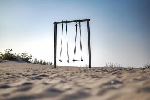 Two empty rustic wooden swings standing on a sandy beach dune against a cle.. Stock Photos