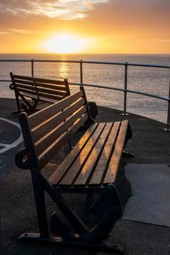 Two empty seaside benches face towards the sea. Amber sunrise Stock Photos