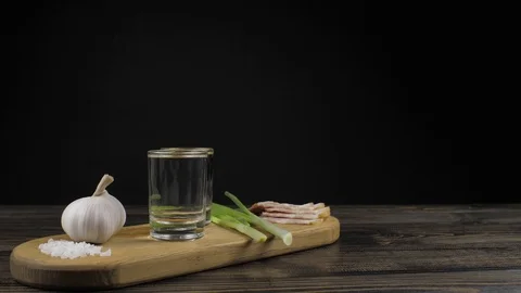 Two empty small faceted glasses for vodka on a wooden board with green onions Stock Footage 120181706