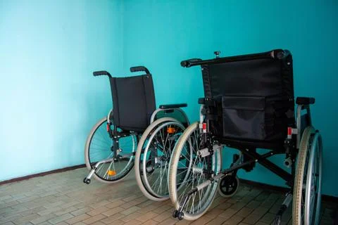 Two empty wheelchairs parked against turquoise wall representing disability and Foto stock