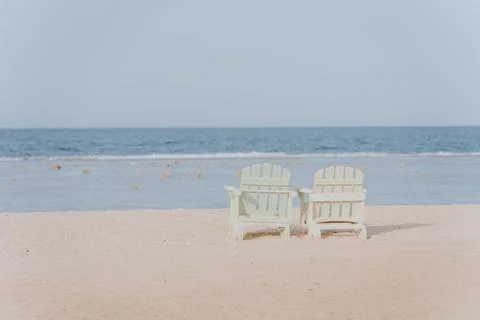 Two empty white beach chairs facing beautiful tropical ocean on sandy beach Stock Photos