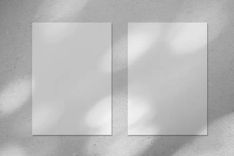 Two empty white vertical poster mockup with diagonal window shadow on the wall Stock Photos