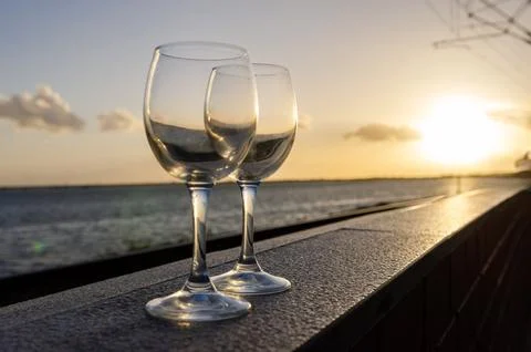 Two empty wine glasses resting on railing at sunset overlooking ocean Stock Photos