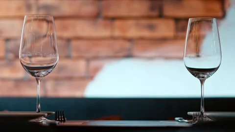 Two empty wine glasses stand ready on a table in front of a brick wall back.. Stock Footage 339752218