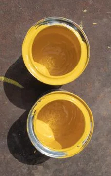 Two empty yellow paint cans with smudges stand on a rusty iron sheet lit by s Stock Photos