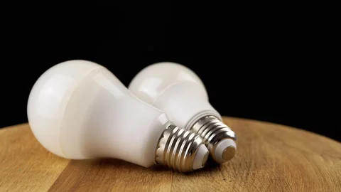 Two Energy Saving Light Bulbs Spin on a Wooden Board, Black Background. Close up Video stock 244416923