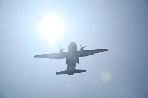 Two-engine airplane flying in the blue sky with sun and lens flare Stock Photos