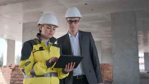 Two Engineer In Helmets With Tablet Device And Big Paper Drawings Discussing Video stock 114533787