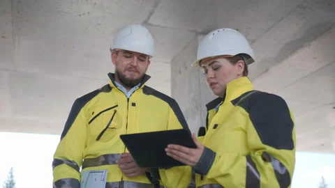 Two Engineer In Helmets With Tablet Device And Big Paper Drawings Discussing Stock Footage 114536133