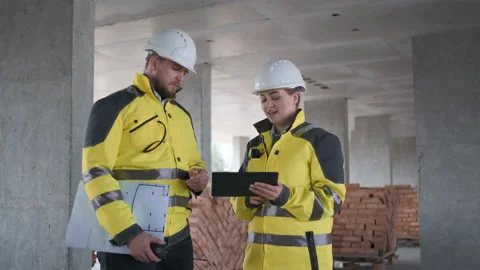 Two Engineer In Helmets With Tablet Device And Big Paper Drawings Discussing Video stock 114536164