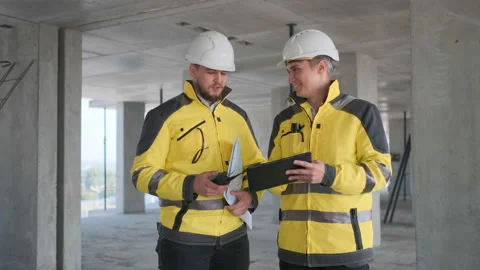 Two Engineer In Helmets With Tablet Device And Big Paper Drawings Discussing Stock Footage 114537928