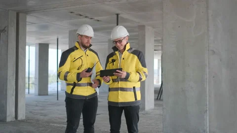 Two Engineer In Helmets With Tablet Device And Big Paper Drawings Discussing Video stock 114538973