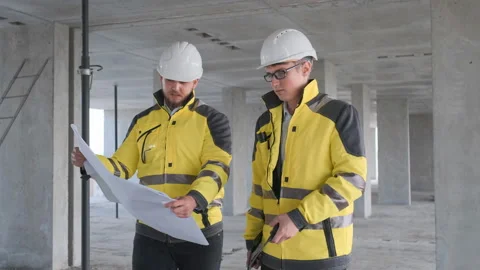 Two Engineer In Helmets With Tablet Device And Big Paper Drawings Discussing Stock Footage 114539927