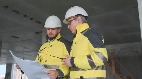 Two Engineer In Helmets With Tablet Device And Big Paper Drawings Discussing Stock Footage 114540223