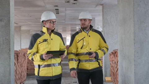 Two Engineer In Helmets With Tablet Device And Big Paper Drawings Discussing Stock Footage 114540866