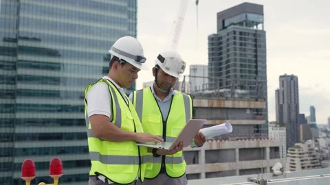 Two Engineer men are standing on a roof, one of them is writing on a laptop.. Stock Footage 280732577