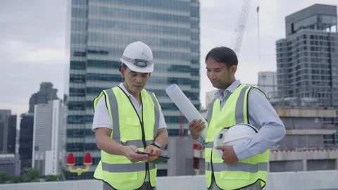 Two engineer men in safety vests are standing on a rooftop. Stock Footage 280732495