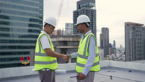 Two engineer men in safety vests walk shake hand on a rooftop, one of them .. Stock Footage 280732590