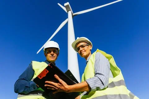 Two engineer workers looking at camera while working in wind turbine field. Stock Photos