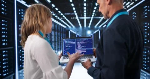 Two Engineers Analyzing Cloud Servers On Laptops In Modern Data Center. Stockfoto's