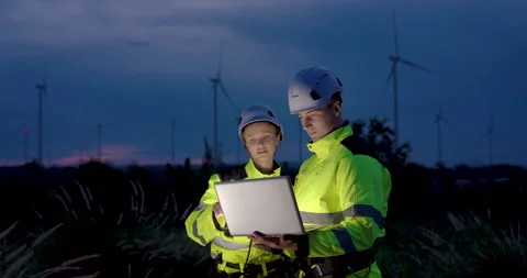 Two engineers analyzing data on laptop at night wind farm, teamwork reviewing Stock Footage 337166718