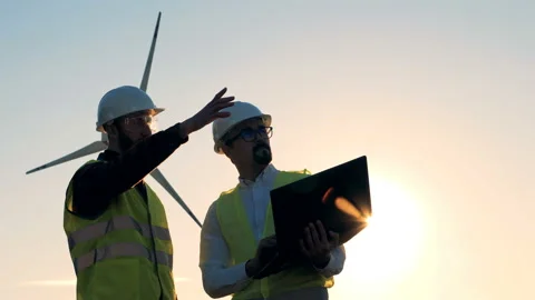 Two engineers are talking in front of a wind turbine in sunlight. Clean, eco Video stock 97986966